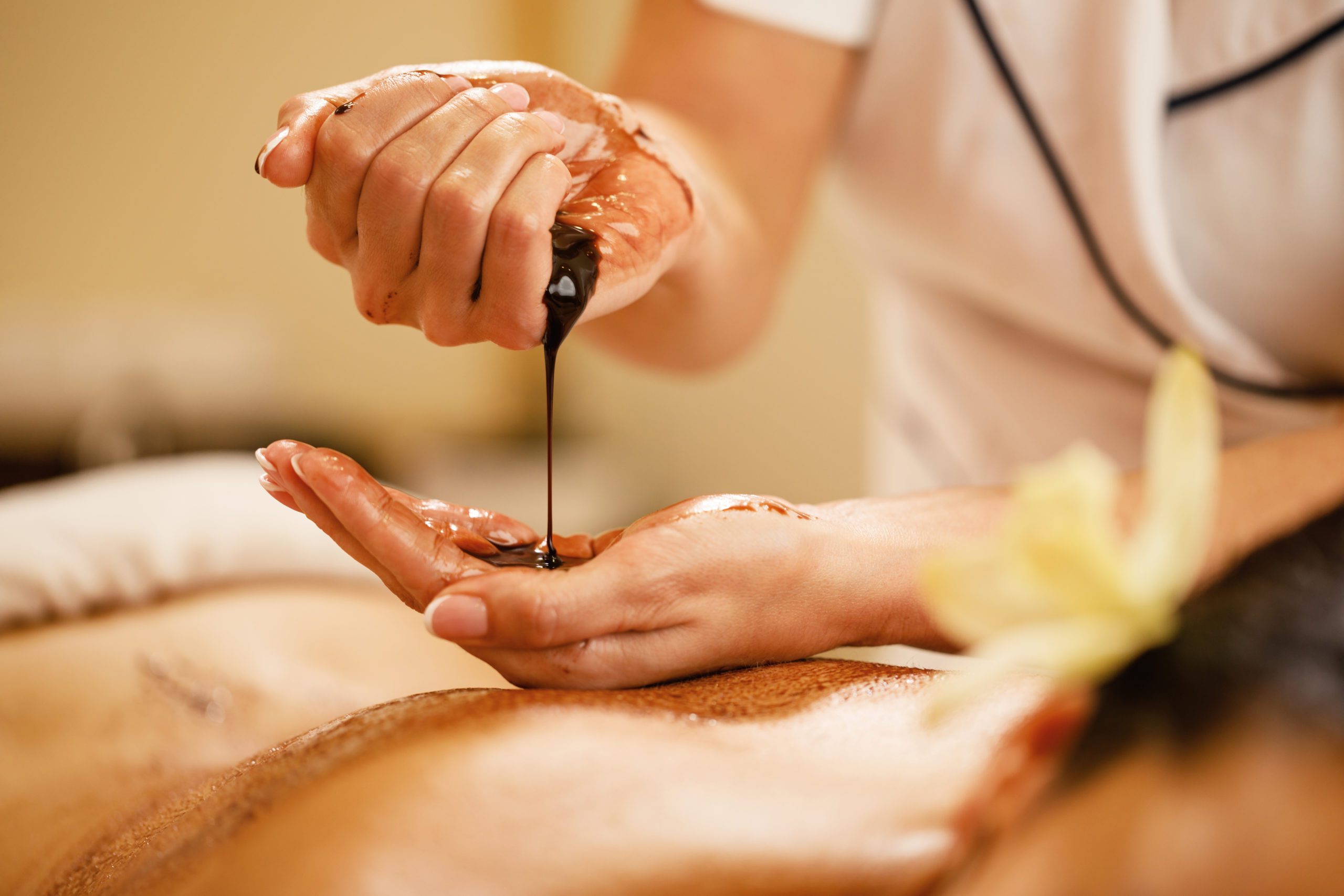 Close-up of therapist preparing for hot chocolate massage at the spa. Close-up of massage therapist pouring hot chocolate in her hands before spa treatment.