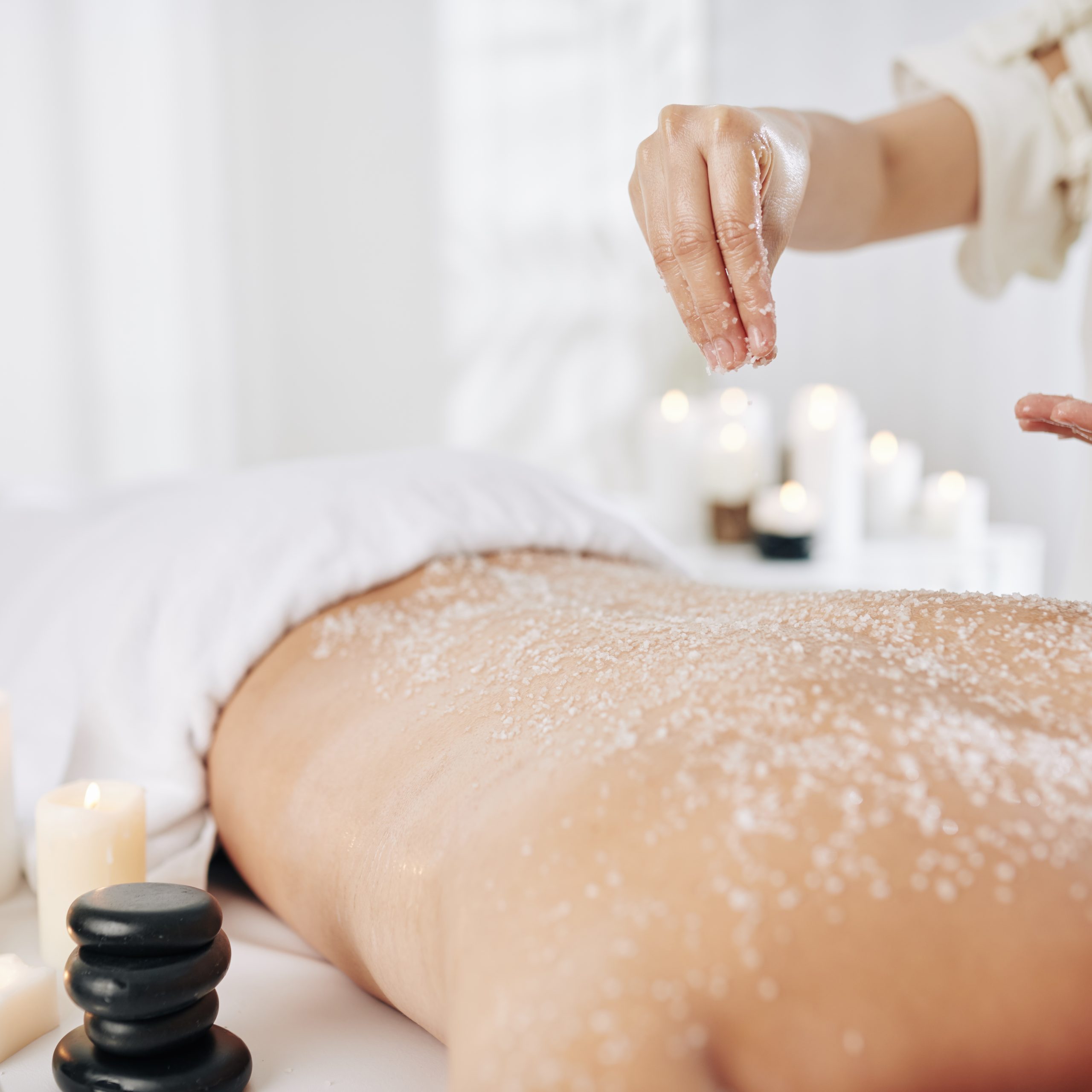 Beautician applying salt scrub Beautician applying salt scrub on back of male client to get rid of dead skin before massage
